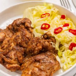 Crispy fried chicken with cabbage and red chili peppers on white plate.