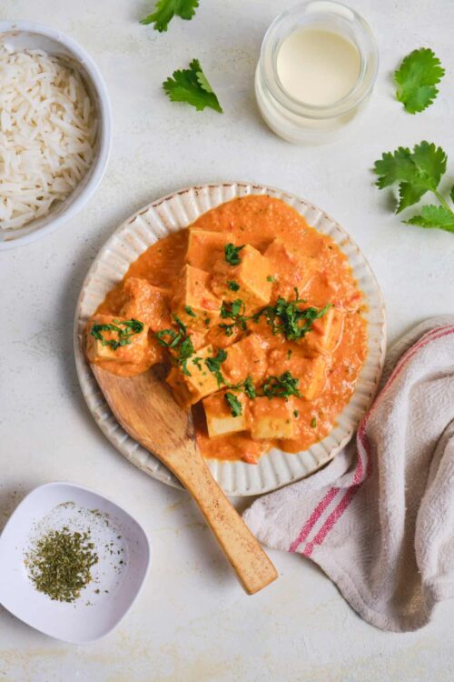 Creamy chicken curry with rice served on a ceramic plate, garnished with fresh herbs.