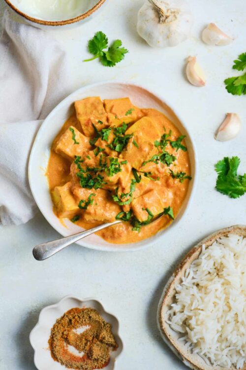 Creamy chicken curry with spices garnished with cilantro and served with white rice.