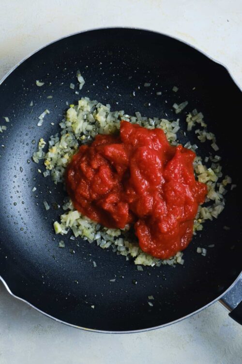 Sautéed onions with tomato sauce in a black non-stick skillet.