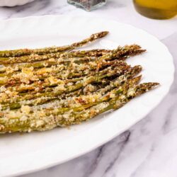 Roasted asparagus with breadcrumbs on a white platter, herbs, olive oil, and parmesan cheese, healthy vegetable side dish.