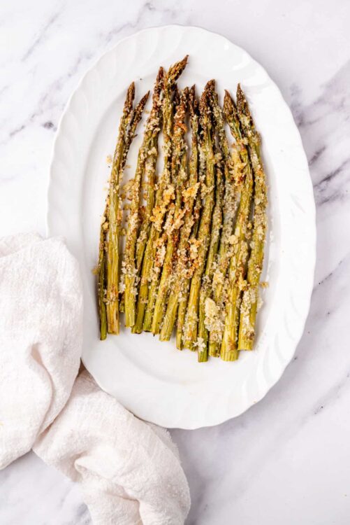 Roasted asparagus with Parmesan cheese on elegant white serving platter.