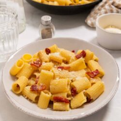 Creamy bacon pasta in a white plate with grated cheese on top.