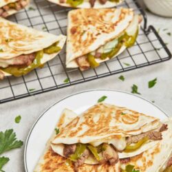 Flank steak quesadilla with green peppers and melted cheese on white plate.
