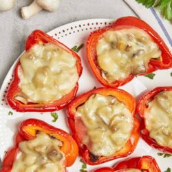 Roasted red peppers stuffed with cheese and mushrooms, baked and served on a white plate.