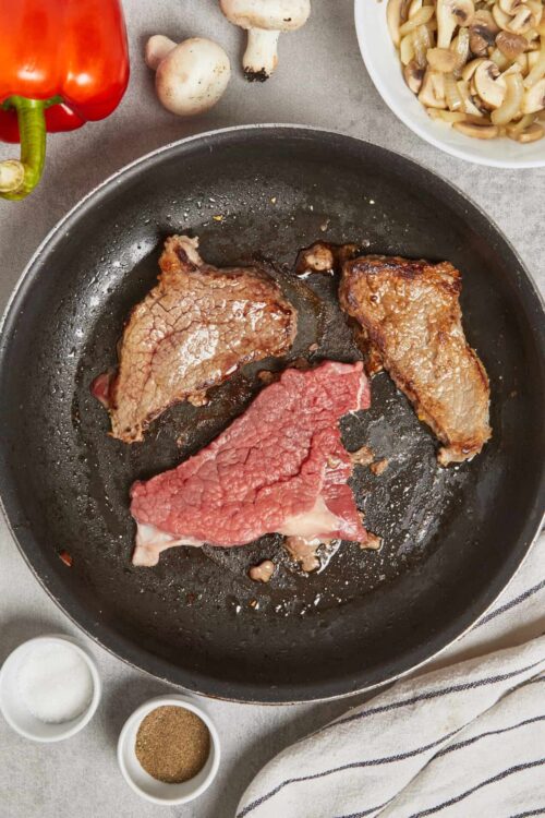 Juicy steaks cooking in a skillet with fresh vegetables and seasonings for savory beef dishes.