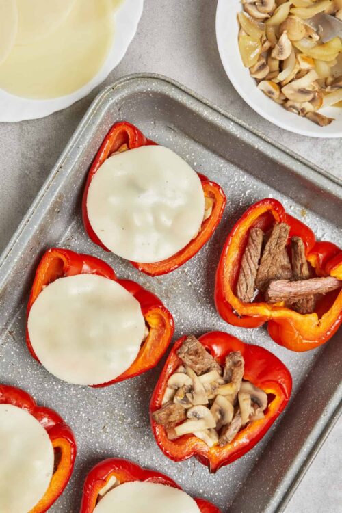 Bell pepper stuffed with beef, mushrooms, and cheese on baking sheet, ready for oven cooking.