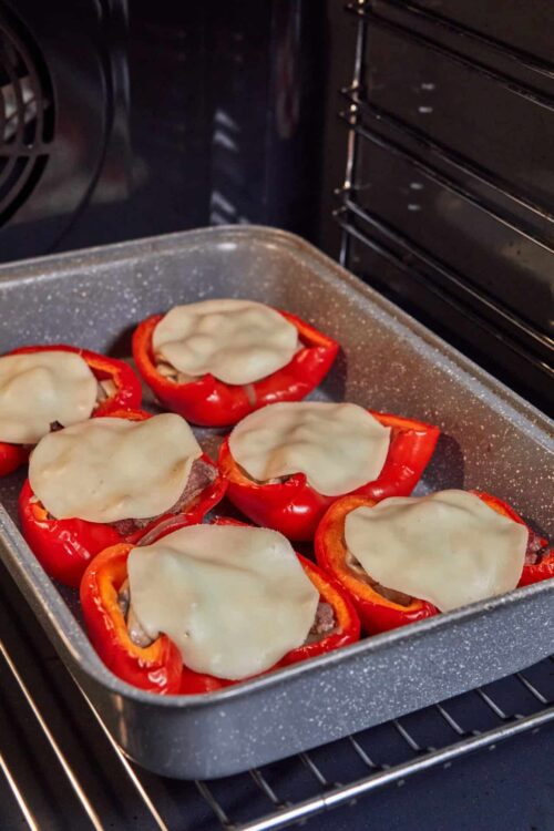 Red bell peppers stuffed with beef and topped with melted cheese in the oven.