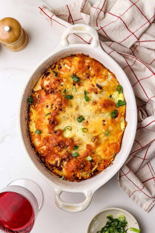 Baked cheesy casserole with green onions in a white baking dish.