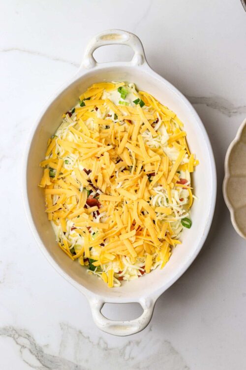 Cheesy casserole with shredded cheese, green onions, and casserole ingredients in a ceramic baking dish.