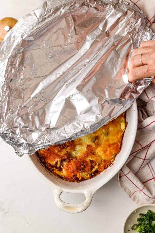Baked lasagna in ceramic dish covered with aluminum foil, ready to serve.