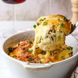 Cheesy baked casserole with green onions and herbs in a white dish, classic comfort food.