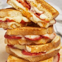 Crispy grilled cheese sandwiches with bacon and melted cheese, stacked tall on a plate.