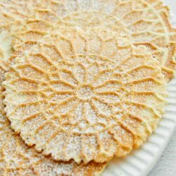 Delicate waffle cookies dusted with powdered sugar on a white plate.