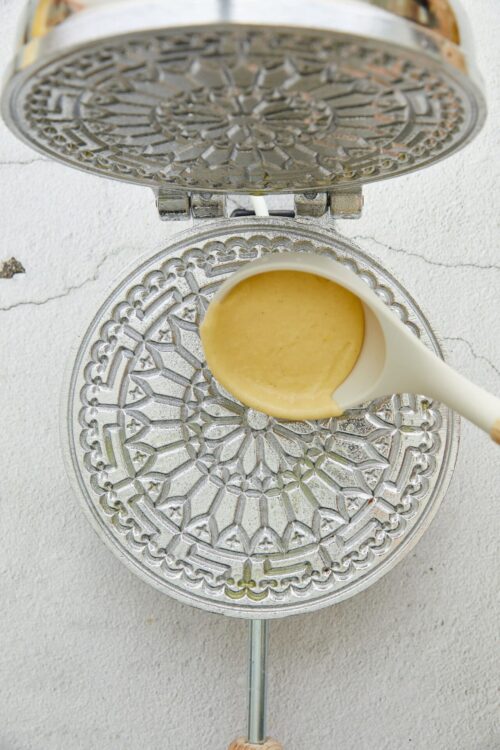 Drizzle batter onto vintage waffle iron for homemade waffles.