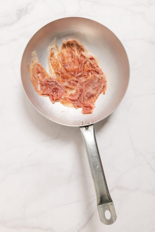 Thinly sliced prosciutto in a stainless steel skillet.