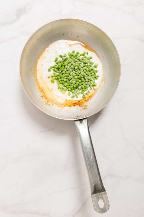 Fresh green peas cooking in a stainless steel skillet with creamy sauce.