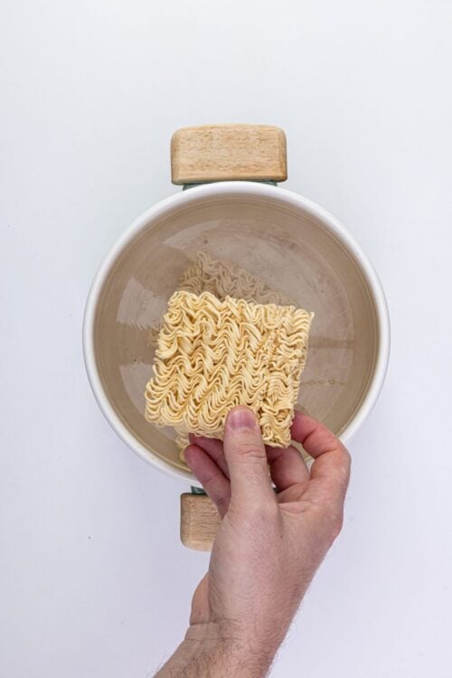 Uncooked instant ramen noodles in a white pot on a white background.