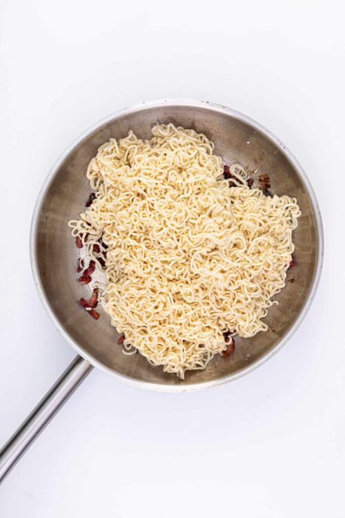 Creamy ramen noodles with crispy bacon in a stainless steel skillet.