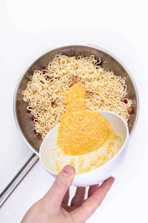 Creamy cheese sauce added to cooked instant ramen noodles in a skillet.