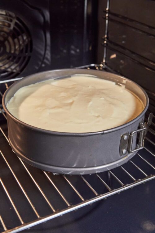 Baked cheesecake batter in a springform pan inside an oven.