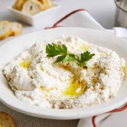 Creamy ricotta cheese dip garnished with parsley on a white plate for appetizers or snacks.