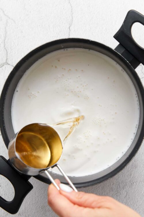 Cream being poured into a pot of milk on a stovetop.