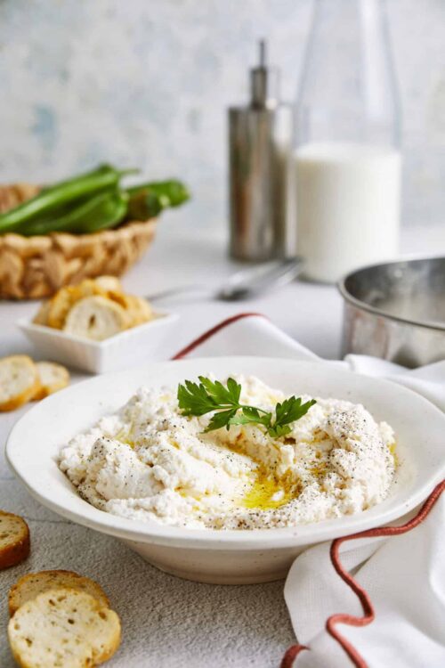 Creamy homemade ricotta cheese with olive oil and fresh parsley on a white plate.