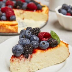 Fresh berry-topped cheesecake with blueberries, blackberries, and raspberries on a white plate.