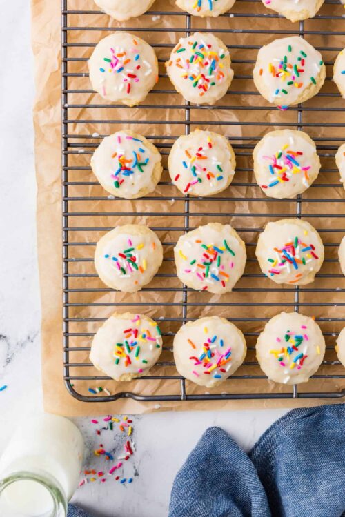 Colorful homemade sugar cookies with white glaze and rainbow sprinkles on a cooling rack.