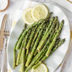 Fresh roasted asparagus with lemon slices on white plate, healthy vegetable dish, vibrant green asparagus, easy side recipe, summer meal idea.