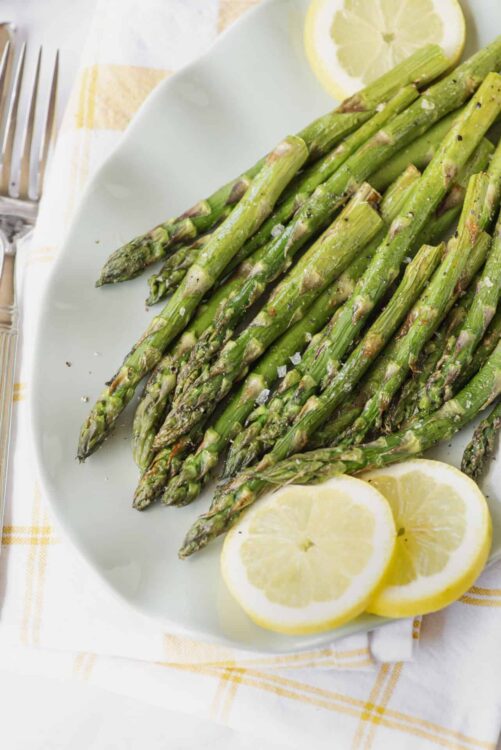 Roasted asparagus with lemon slices on a white plate, healthy vegetable side dish, fresh green asparagus.