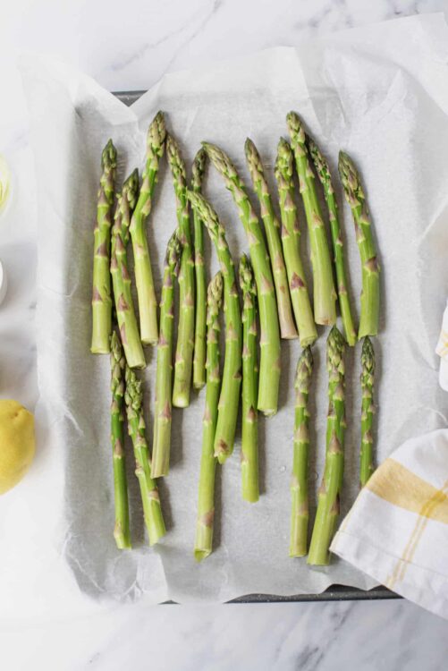 Fresh roasted asparagus spears on parchment paper for easy baking and healthy meal preparation.