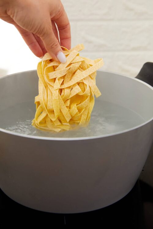 Cooking fresh pasta in a gray pot with boiling water, hand lifting pasta, making homemade pasta from scratch.