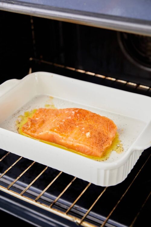 Seasoned salmon fillet in a white baking dish on oven rack.