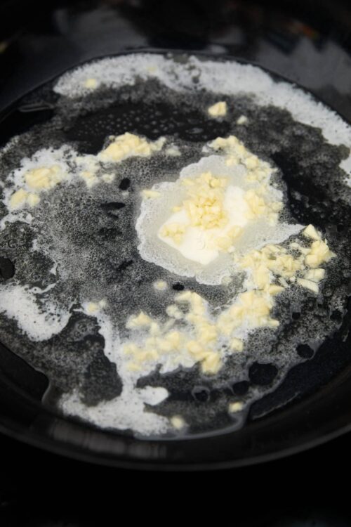Cream cheese and butter melting in a black skillet for baking.