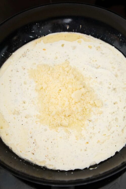 Creamy alfredo sauce with grated Parmesan cheese in a skillet.