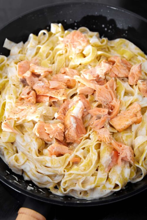 Creamy salmon fettuccine served in a black skillet with tender pasta and flaky cooked salmon.