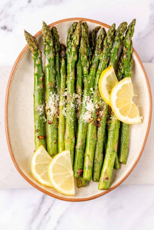 Roasted asparagus with lemon slices and grated cheese on ceramic platter.