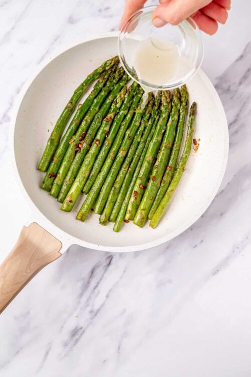 Fresh roasted asparagus with garlic and red pepper flakes in a white skillet.