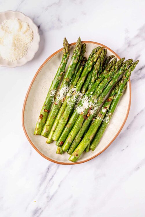 Roasted asparagus with Parmesan cheese on a white dish.