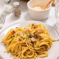 Creamy shrimp and bacon pasta dish on a white plate with parsley garnish.