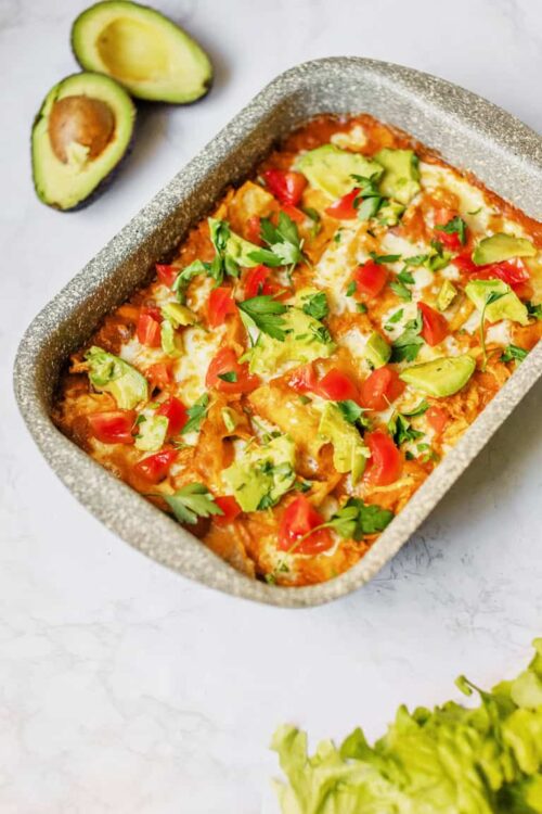 Baked avocado chicken casserole with tomatoes and cheese in grey baking dish.