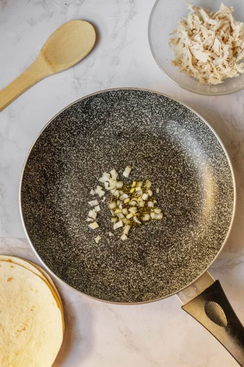 Sautéed onions in a non-stick skillet with a marble countertop background.