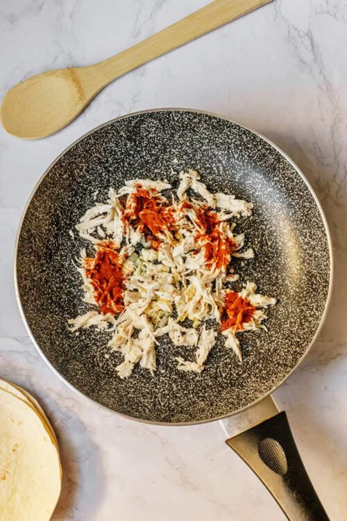 Cooked shredded chicken with salsa in a non-stick skillet on marble countertop.