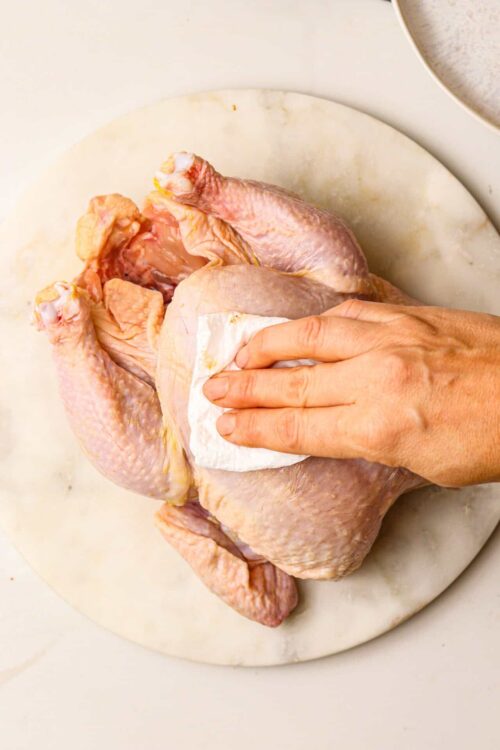 Raw whole chicken on cutting board being prepped for cooking.