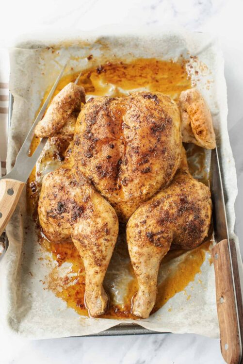 Juicy roasted chicken with crispy skin freshly baked on a baking sheet.