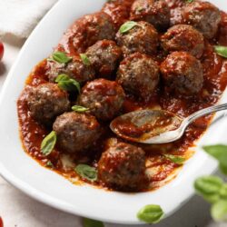 Savory Italian-style meatballs in marinara sauce on white platter with fresh basil.