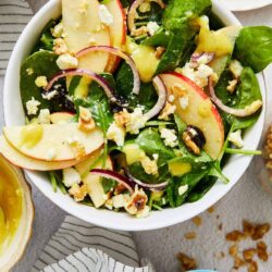 Fresh spinach and apple salad with blue cheese crumbles and walnuts, perfect healthy side dish.