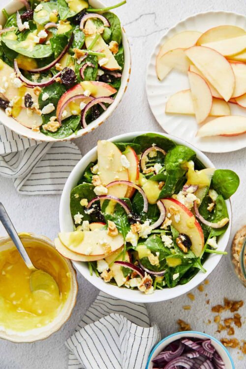 Fresh spinach, apple, and feta cheese salad with walnuts on white bowls, healthy and delicious recipe from Baked Bree.